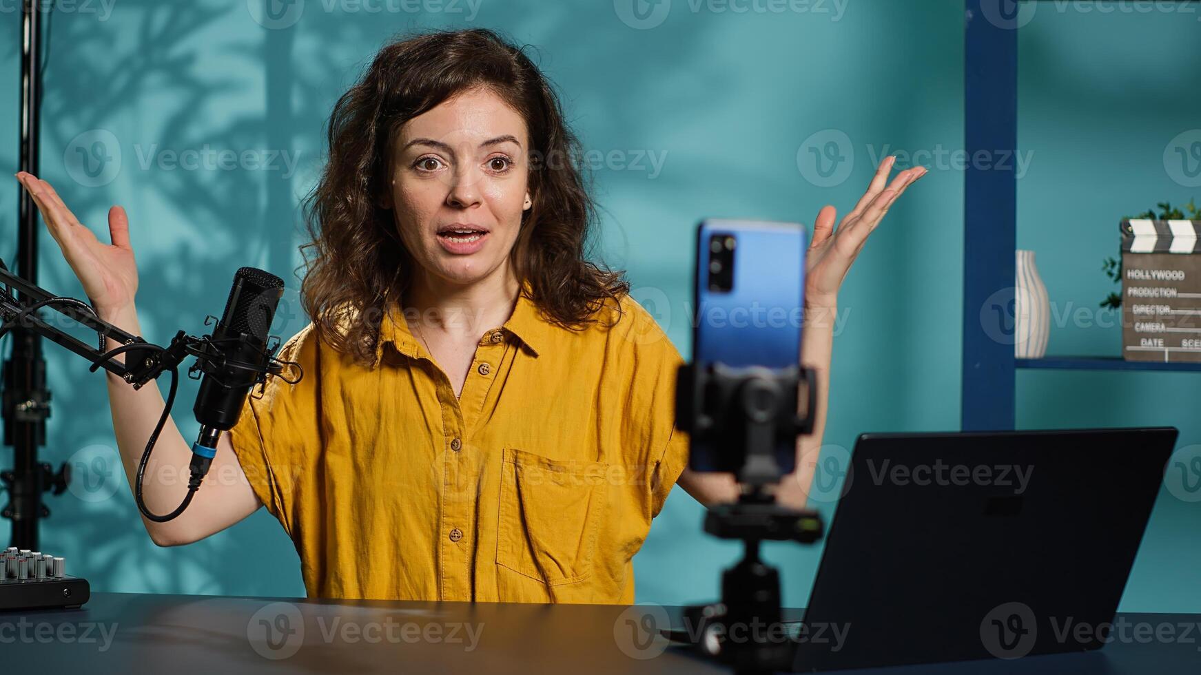 Streamer doing live broadcast on smartphone on holder, talking to audience about recent news headlines. Media star talking with viewers, presenting facts in entertaining manner, camera A photo