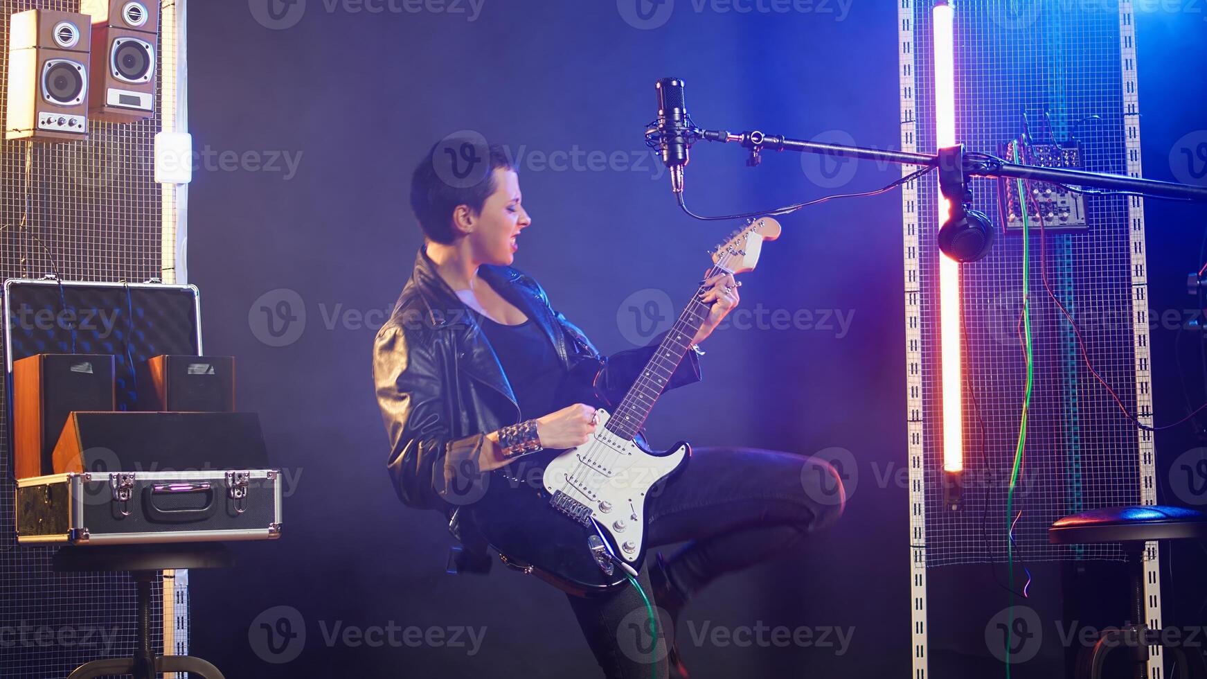Female recording artist playing bass guitar in a nightclub concert, wearing a leather jacket and performing live with edgy bold attitude. Heavy metal musical talent in the studio. Camera A. photo