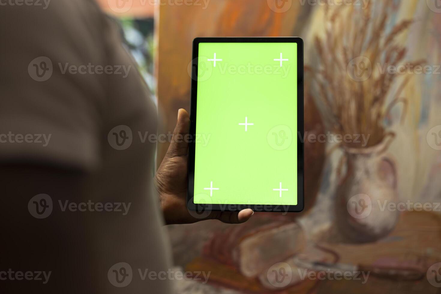 African american artist holding device with green screen mockup in art studio, working on a new painting with a certain technique. Painter using watercolor and acrylic dye for his creation. photo