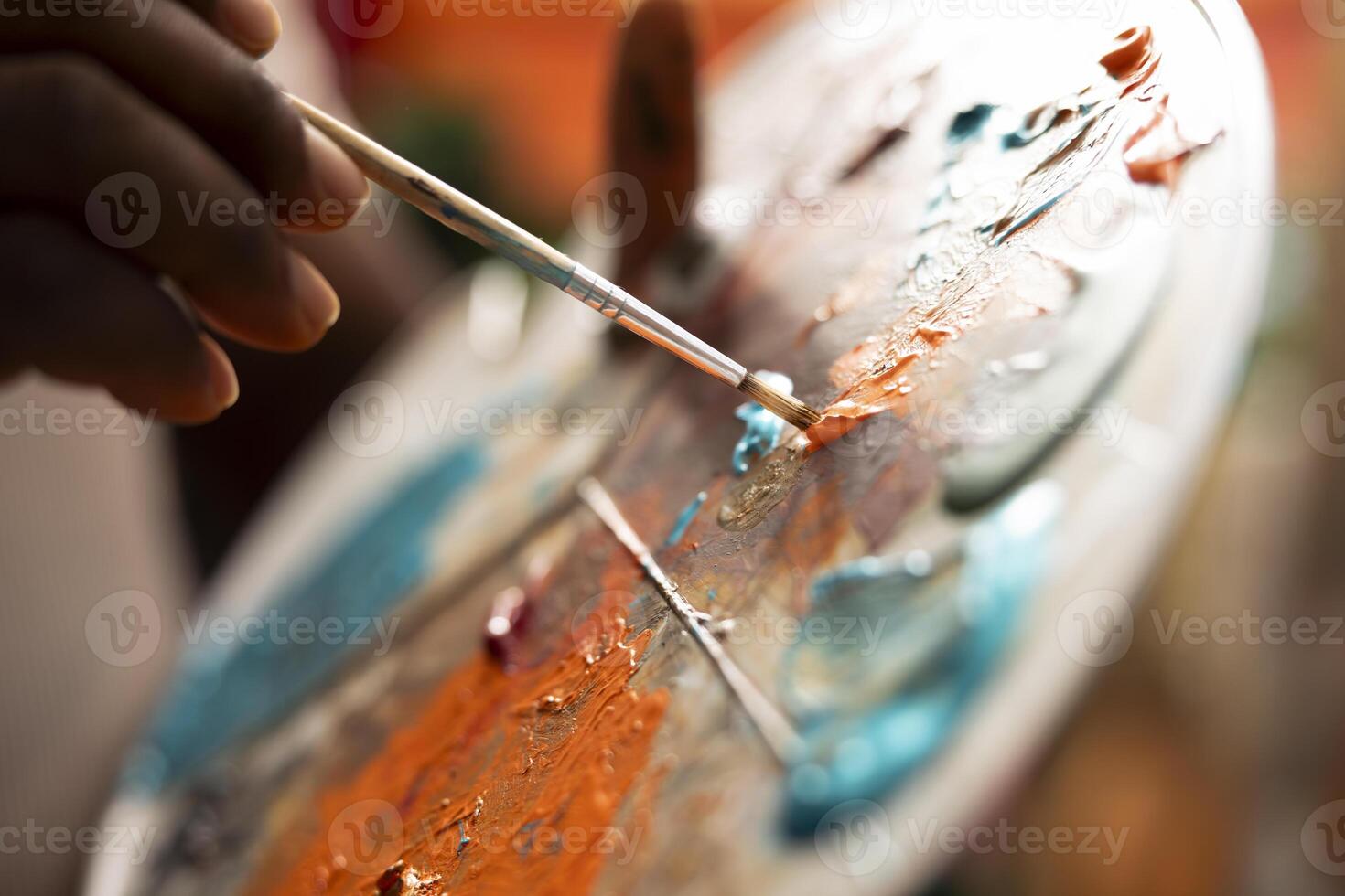 In an art studio, painter mixes multiple watercolor paints on a palette to create a new artwork on canvas. Skilled man painting with tools and showing his imagination, artistic creation. Close up. photo