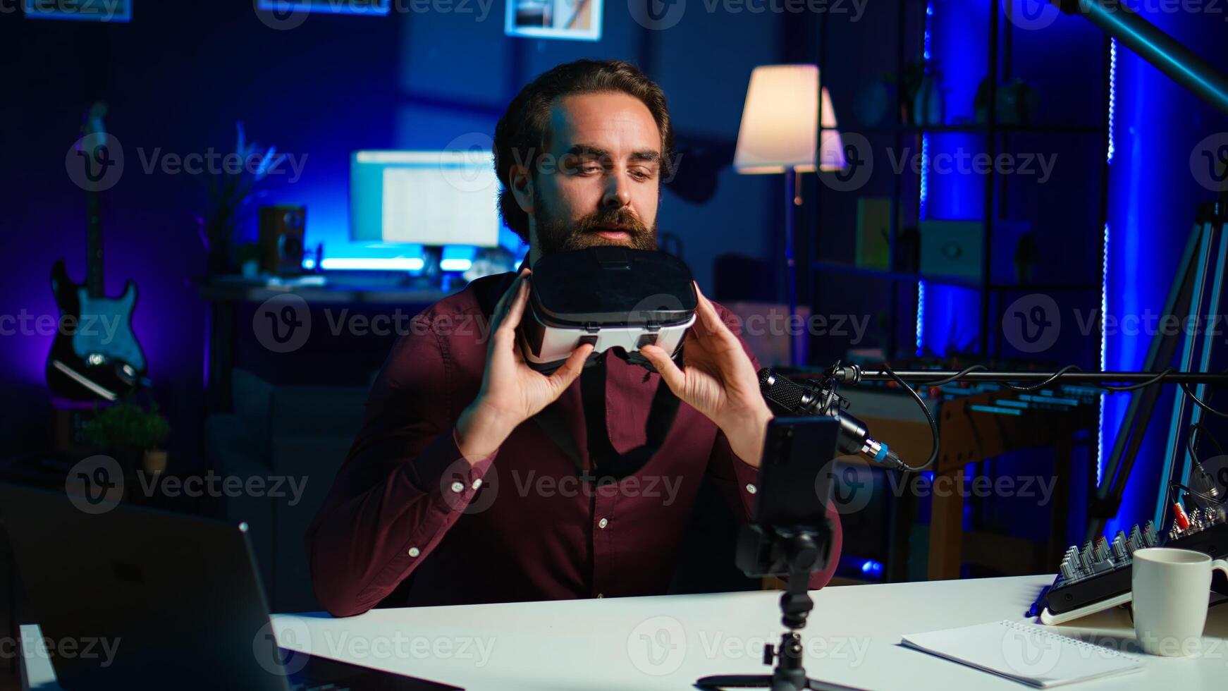 Media star in neon lit studio presents VR goggles from brand sponsoring , closely analyzing features. Influencer reviewing virtual reality headset for tech enthusiasts watching, camera B photo