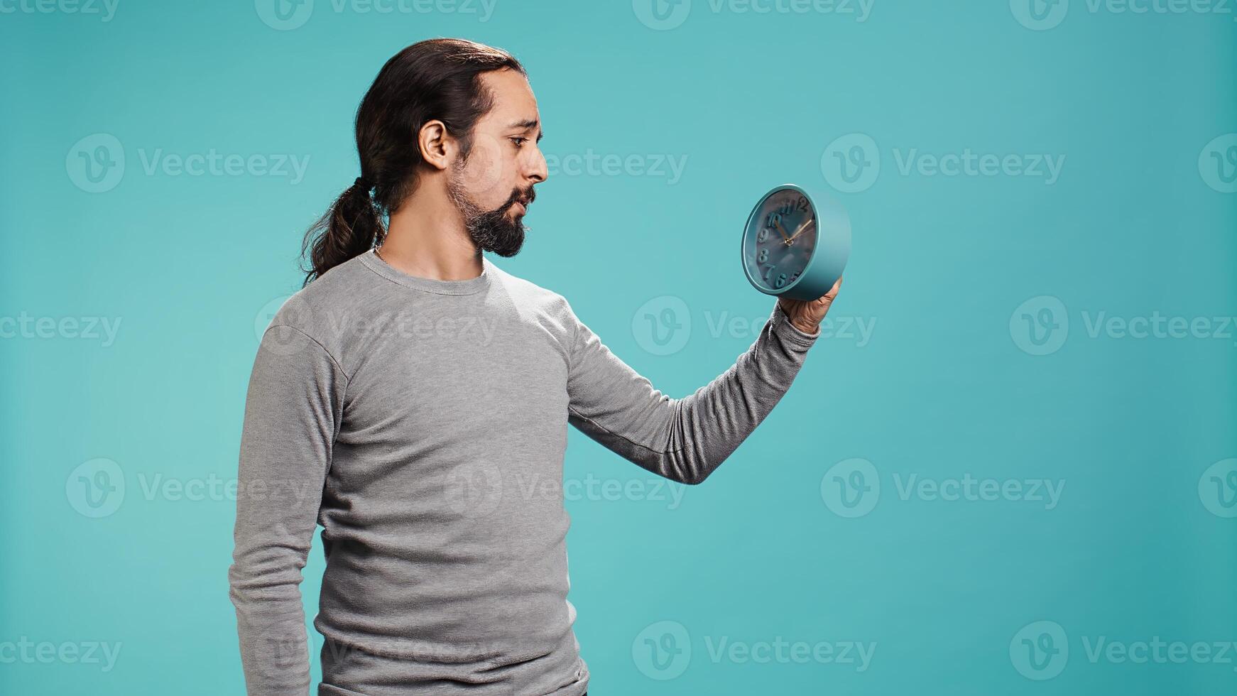 Portrait of worried man looking at alarm clock, stressed after not hearing ring and waking up late in the morning. Anxious person running out of time, isolated over studio background, camera B photo