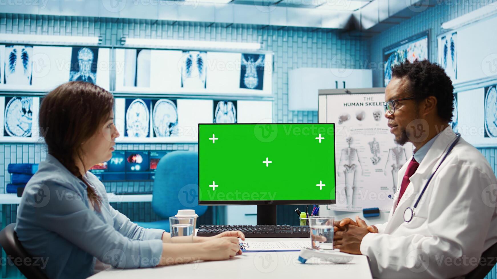 African american medical expert looking at copy space screen with a patient, attending a consultation in cabinet at facility. Male specialist recommending a treatment on health insurance. Camera B. photo