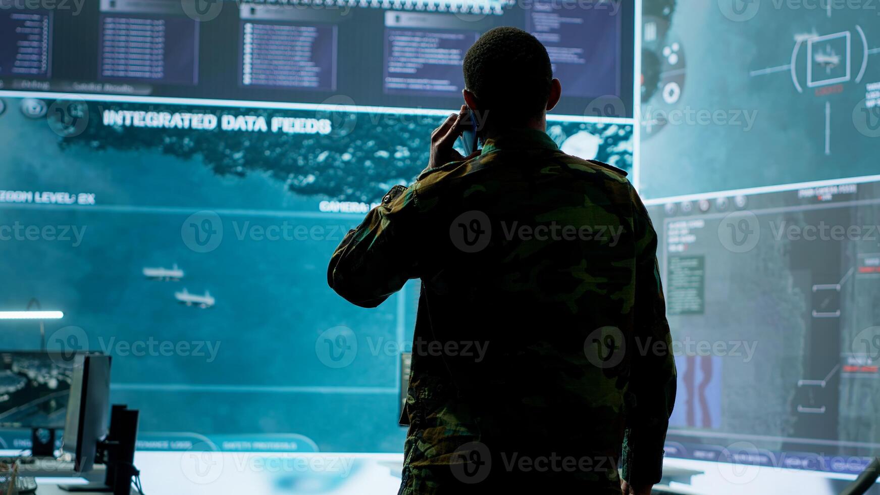 Military man answers phone call in a mission control center, working with advanced technology and satellite imagery to track potential threats and real time data. Intelligence activities. Camera A. photo
