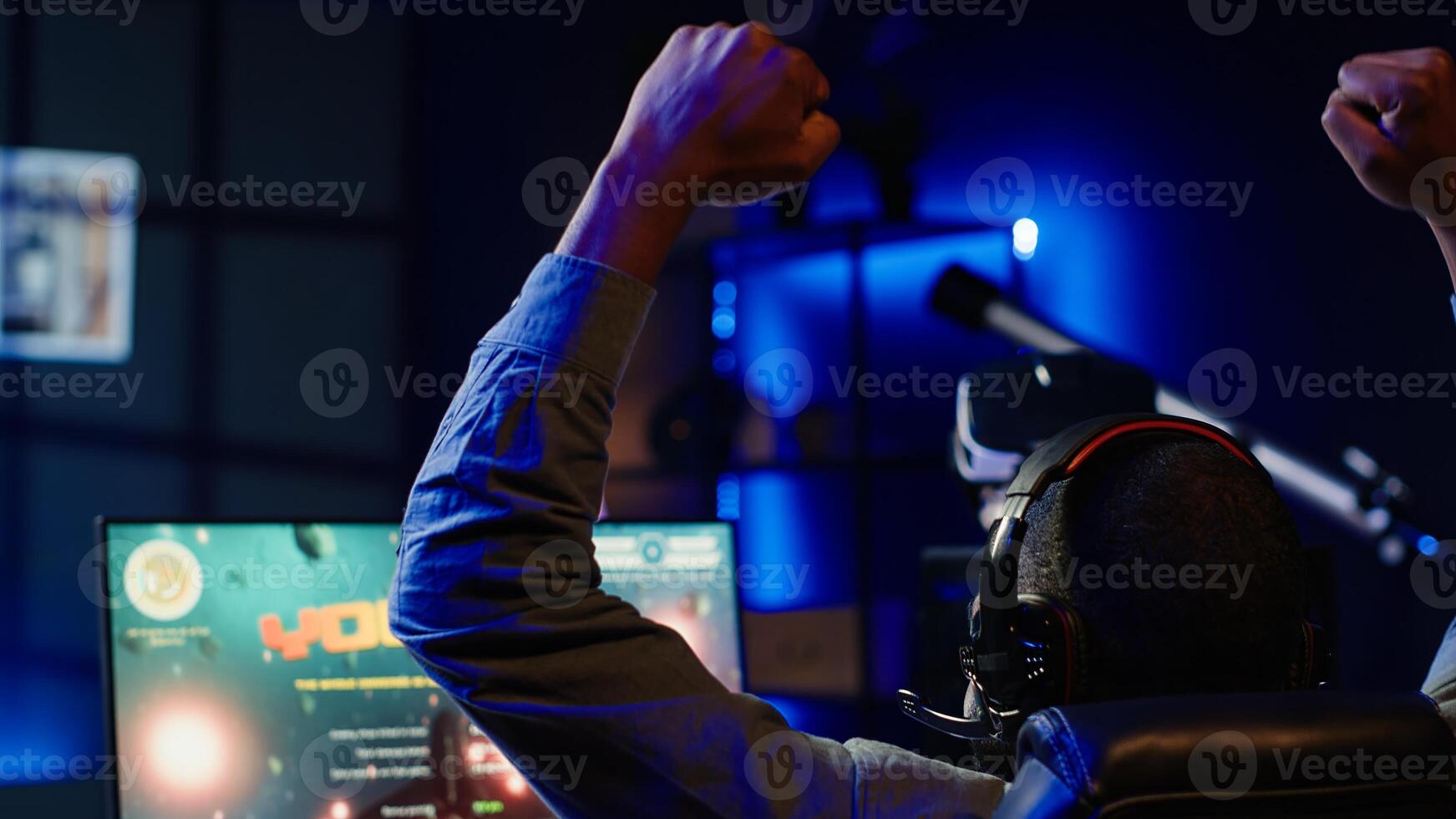 Delighted man celebrates after achieving victory in science fiction videogame at home. Joyous gamer throwing fists in air from excitement after winning SF game on gaming PC, feeling relieved, camera A photo
