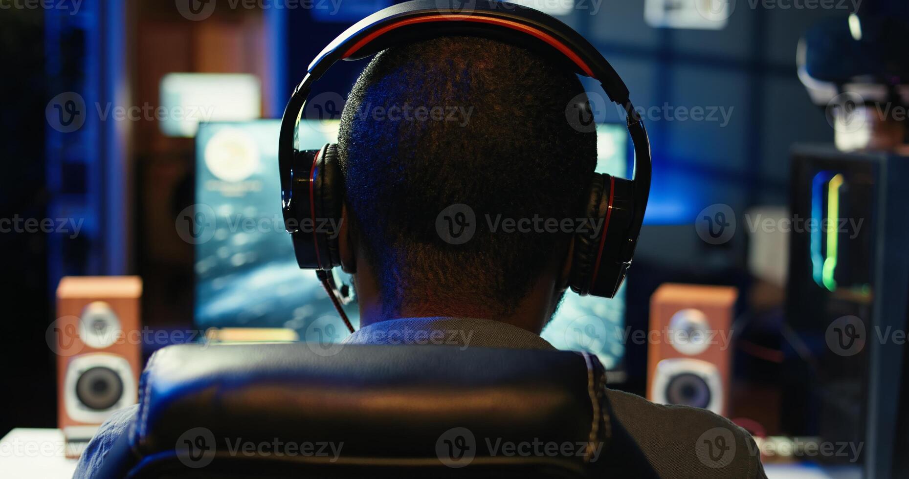 African american player in neon illuminated apartment paying close attention to computer screen during videogame competitive match. Person competing in internet esports tournament, camera B photo