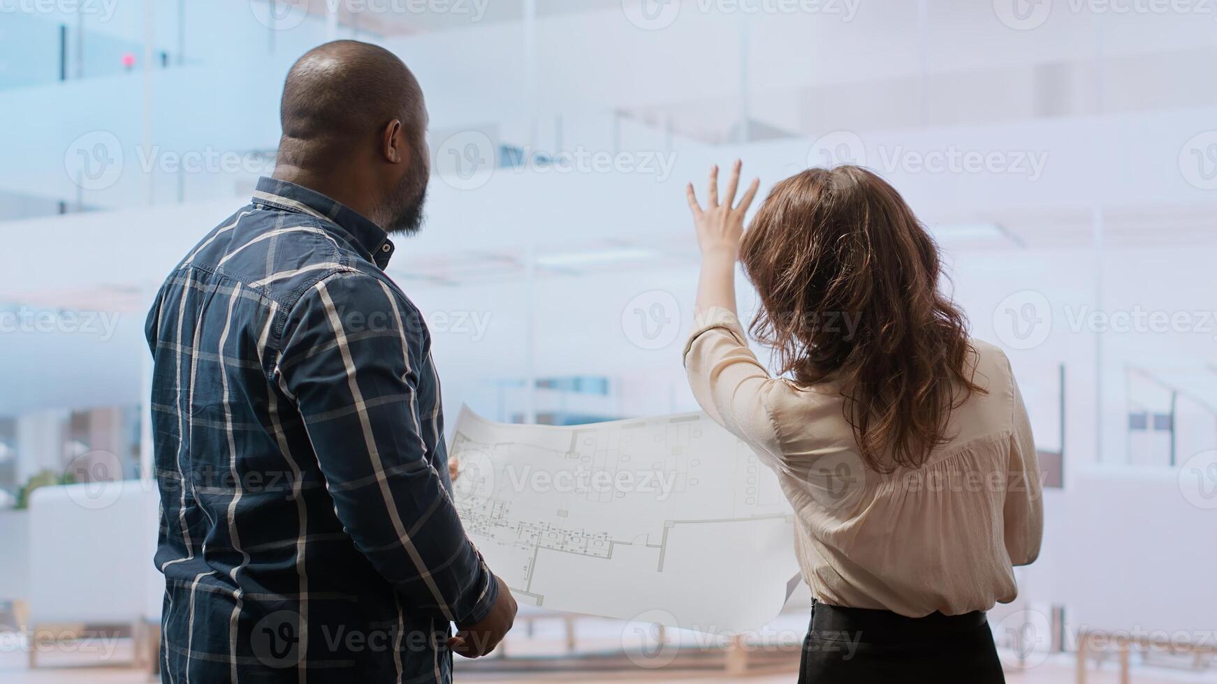 Businesswoman explaining her renovation vision on plans, studying blueprints and discussing layout with the construction manager. Planning a real estate property investment. Camera B. photo
