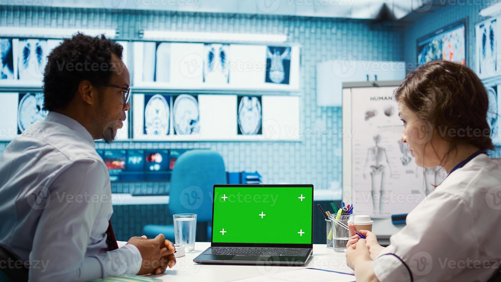 Doctor consulting a male patient in medical facility next to green screen, using modern technology for scan interpretation and diagnostics. Medic gives professional advice based on illness. Camera B. photo