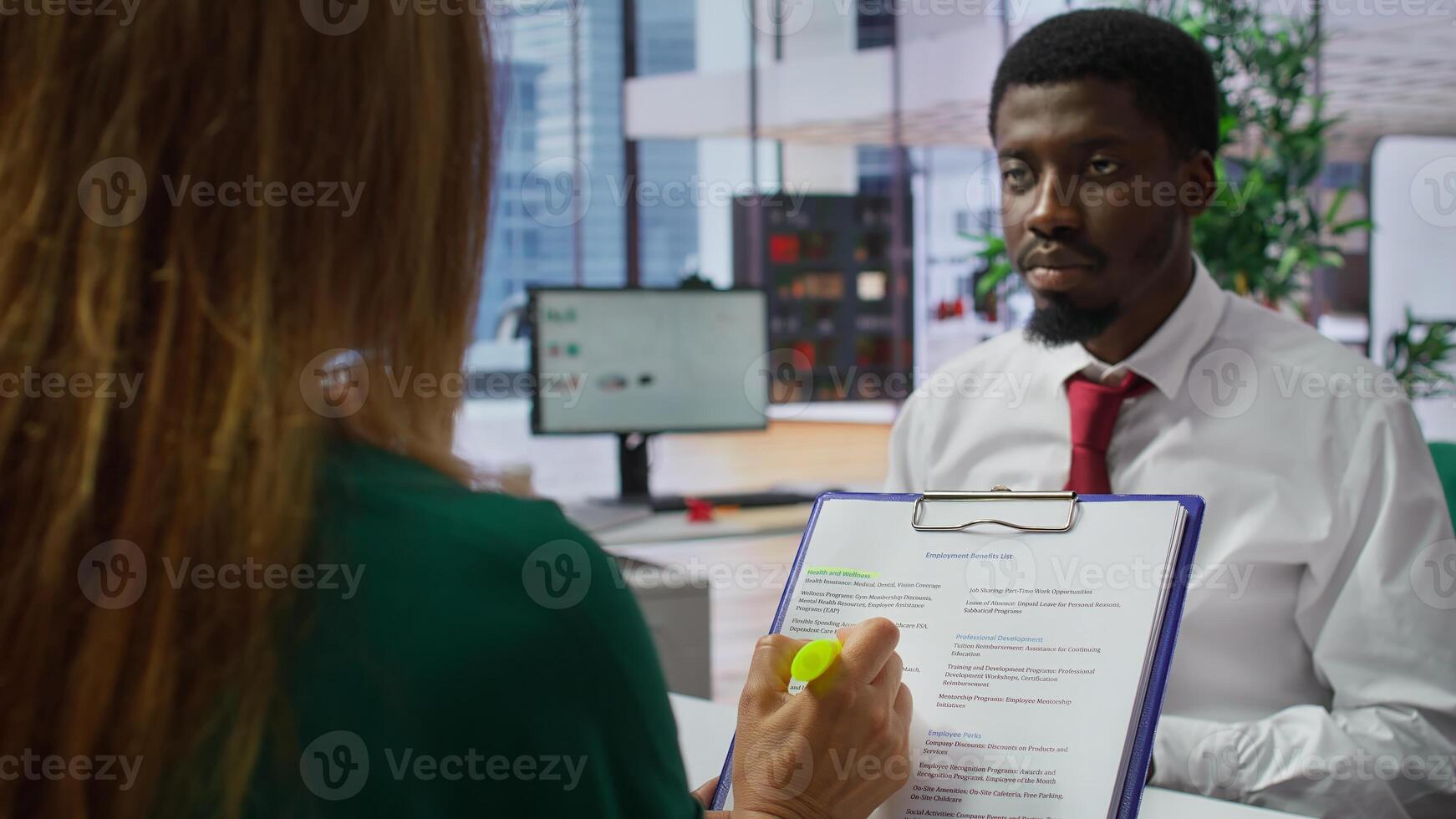 HR staff and applicant discussing the employment contract terms during the interview, providing explanations and clarifications. Job candidate reading the work agreement in high end office. Camera B. photo