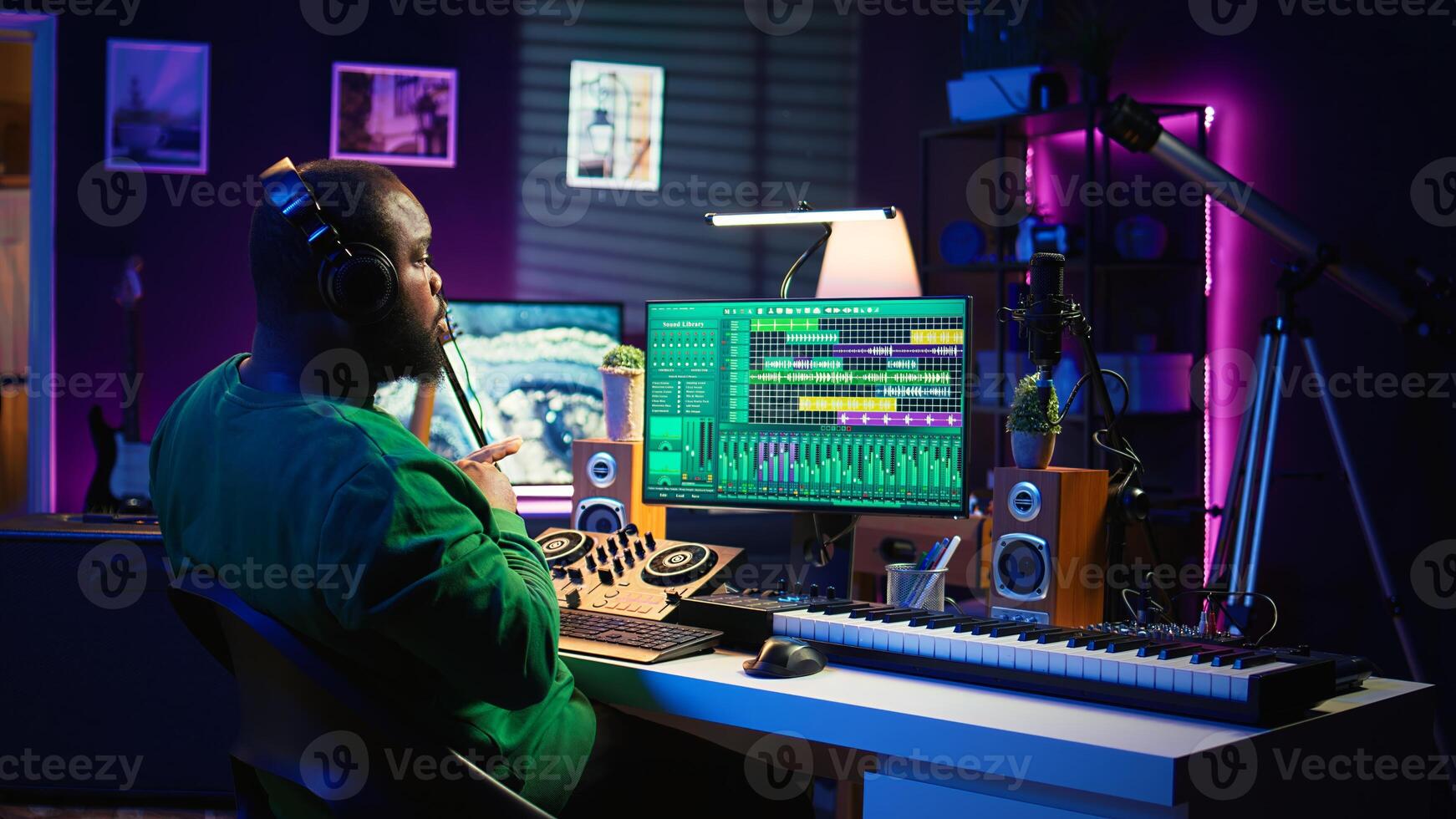 Confident music composer mixing sounds on digital audio software, creating a cool atmosphere in his home studio. Young cheerful producer composing new soundtracks with stereo gear. Camera B. photo