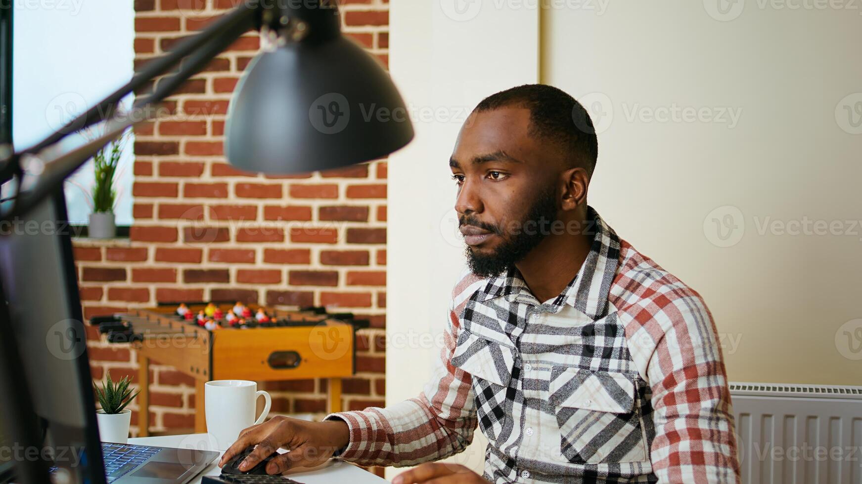 Male coder works from home typing code on a laptop in a modern living room. African american IT engineer using programming language and cloud computing for software development. Camera A. photo