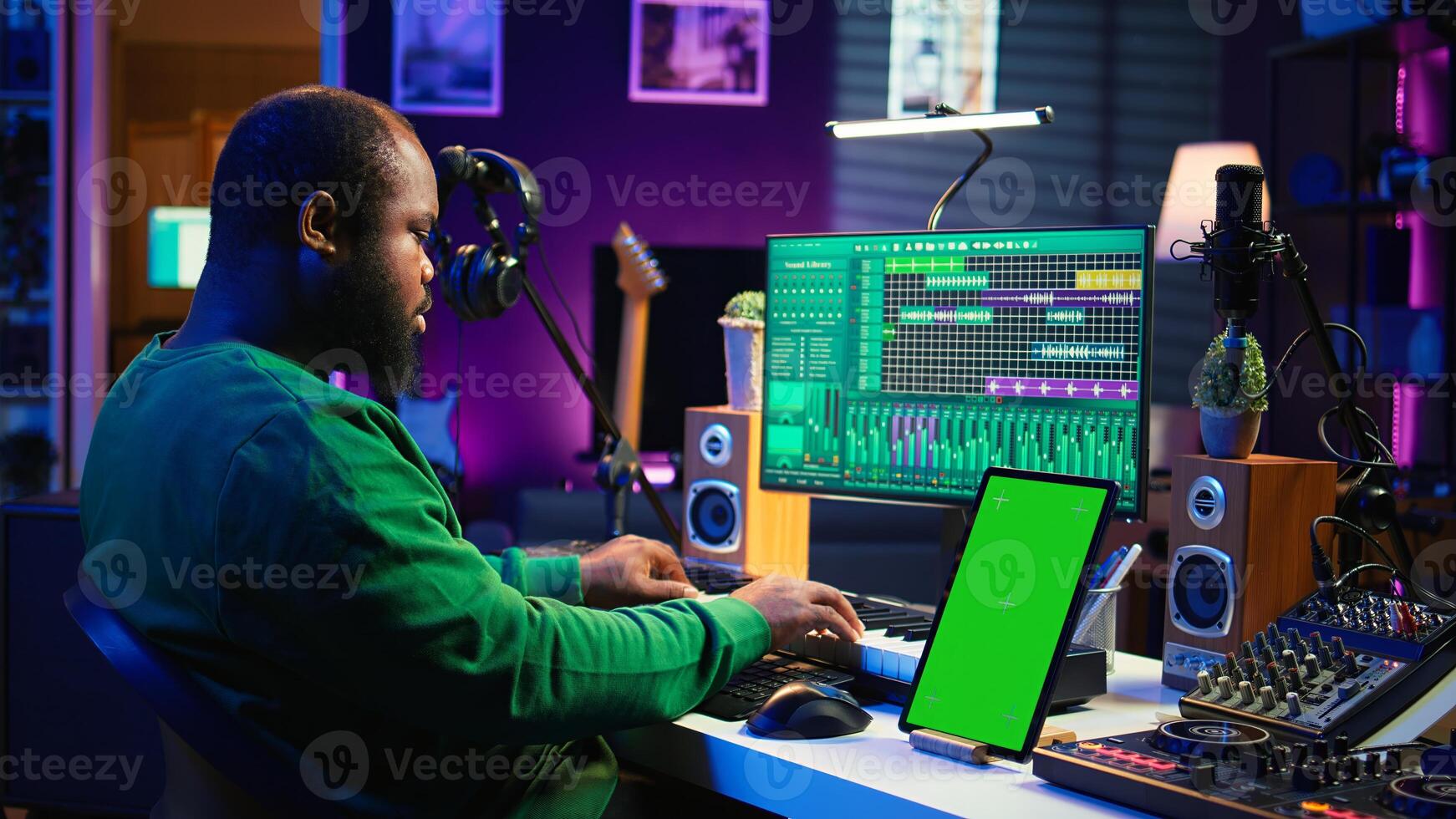 Young musician mixing and mastering songs next to isolated mockup display, operating on digital audio software to add sound effects on new tracks recorded. Audio engineer in home studio. Camera B. photo