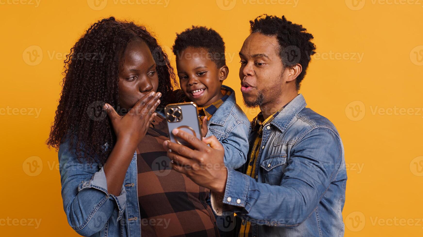 Cute happy family with a young kid take pictures on smartphone, carrying their son and sharing embrace in studio. African american parents feeling grateful for their toddler. Camera A. photo