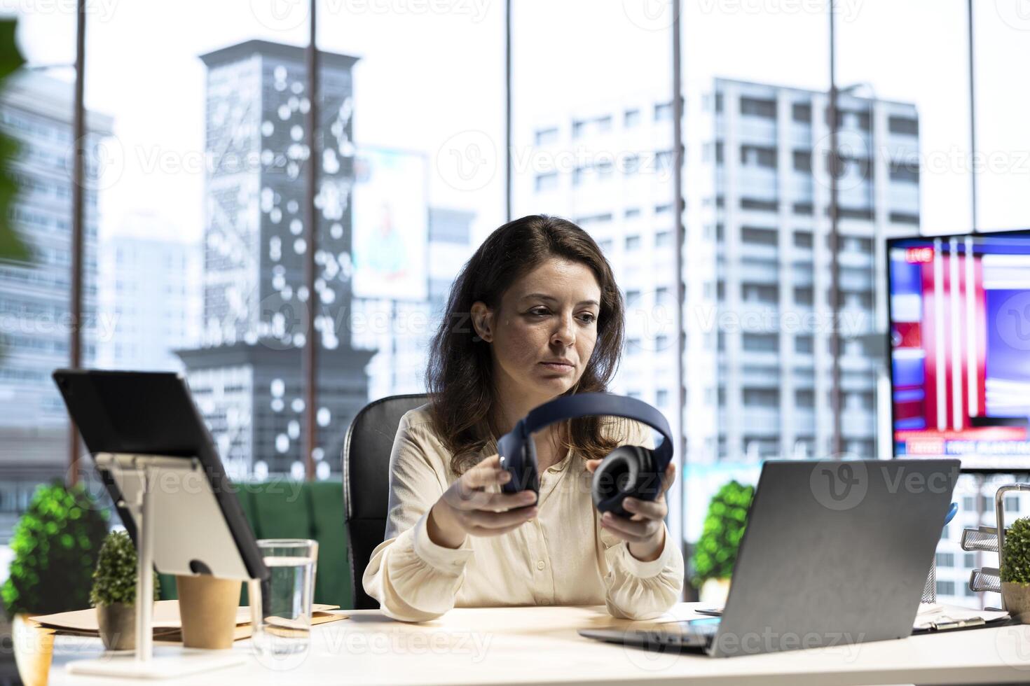 Joyful female CEO working on her business and listening to audiobook, using headset and multitasking in smart urban office. Confident entrepreneur having fun with interesting podcasts, office life. photo