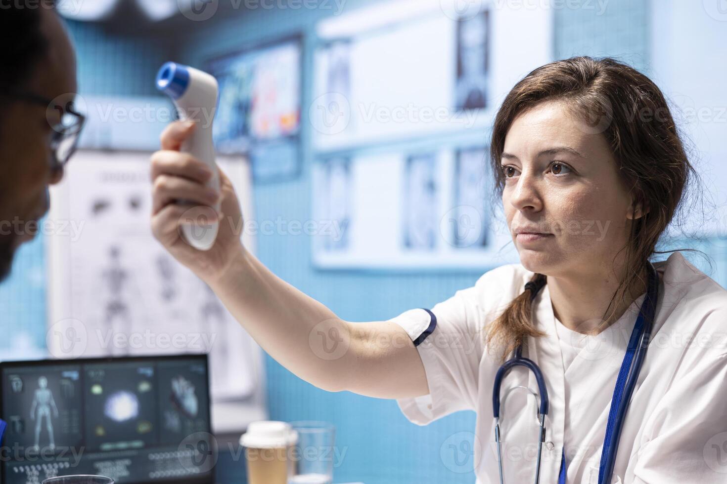 Healthcare specialist using thermometer to check fever measurements, taking temperature levels at a medical consultation. Young medic using digital instrument for diagnostic reports. photo