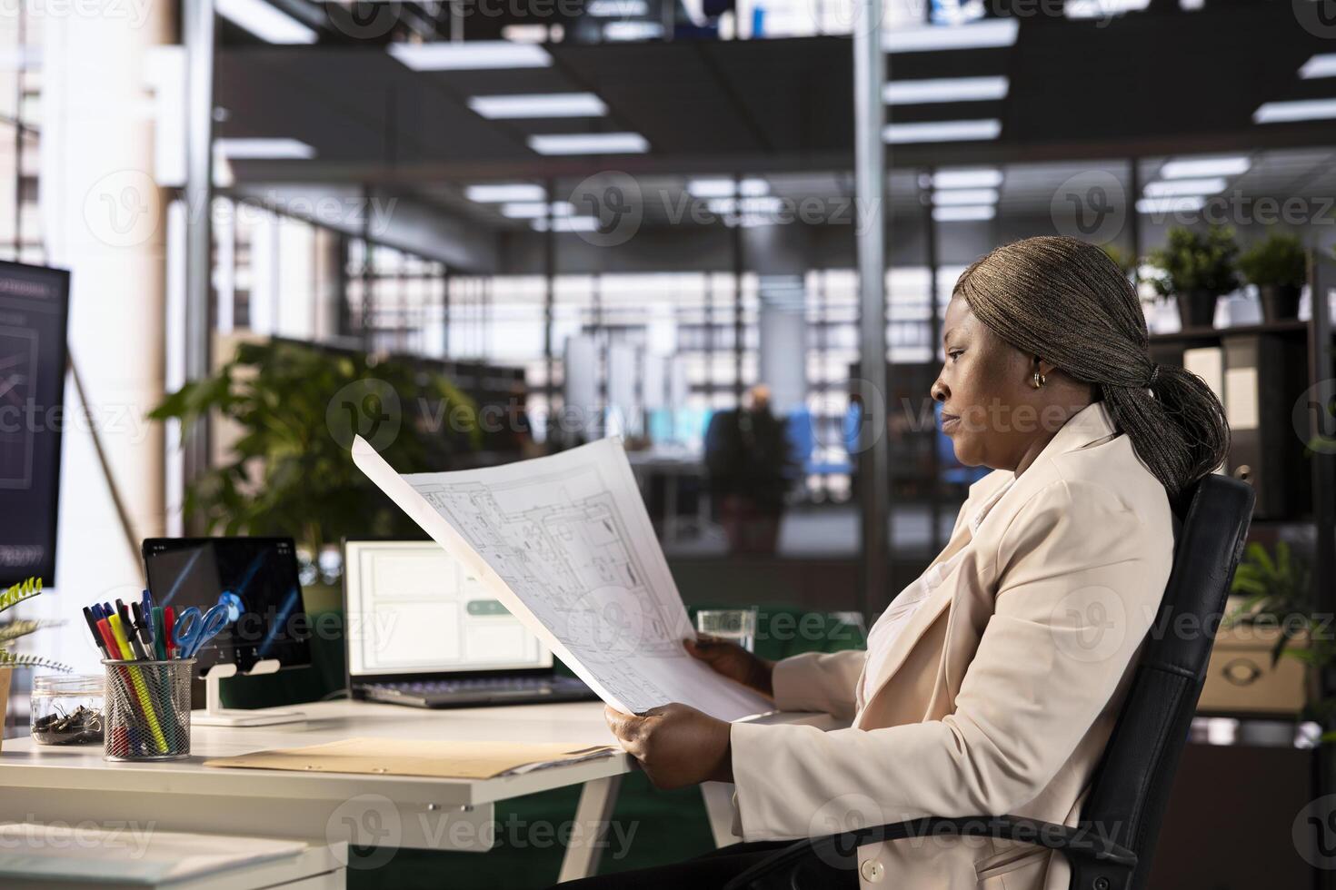 Architect building contractor doing housing development, working in construction industry, African american real estate developer at desk in office looking over architectural floor plan photo