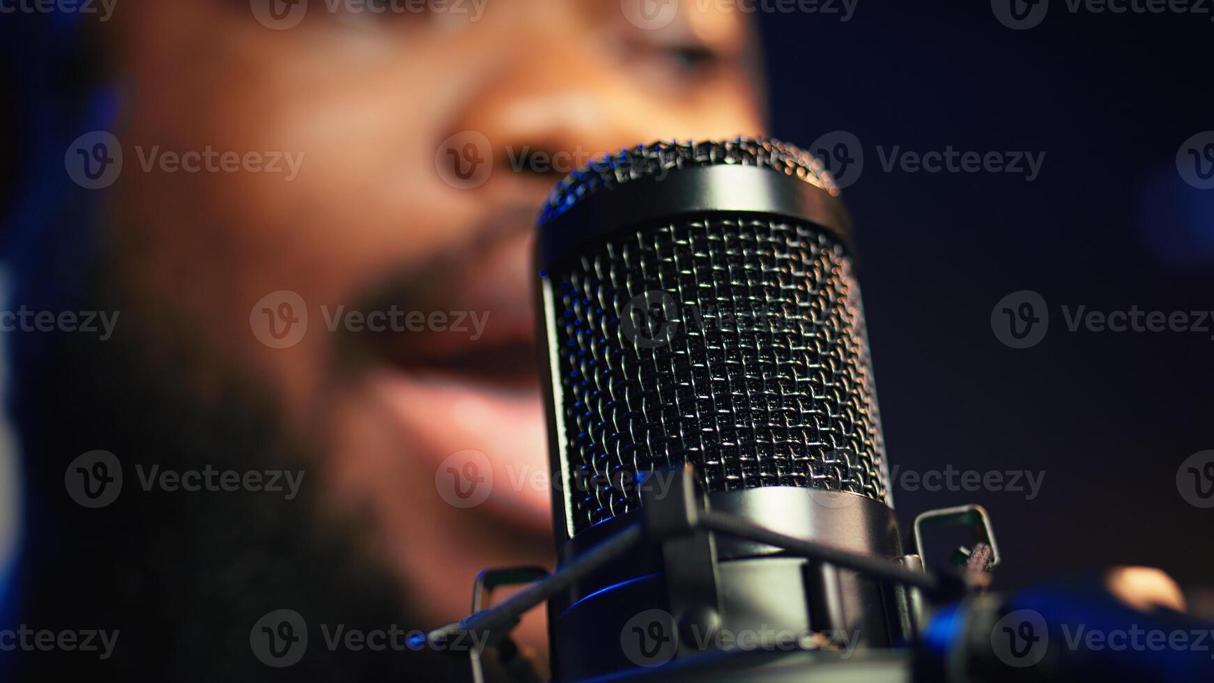 Artist records his voice on microphone in home studio singing a song composed by him. Skilled musician using recordings and lyrics to edit in post production, mixing and mastering session. Camera B. photo