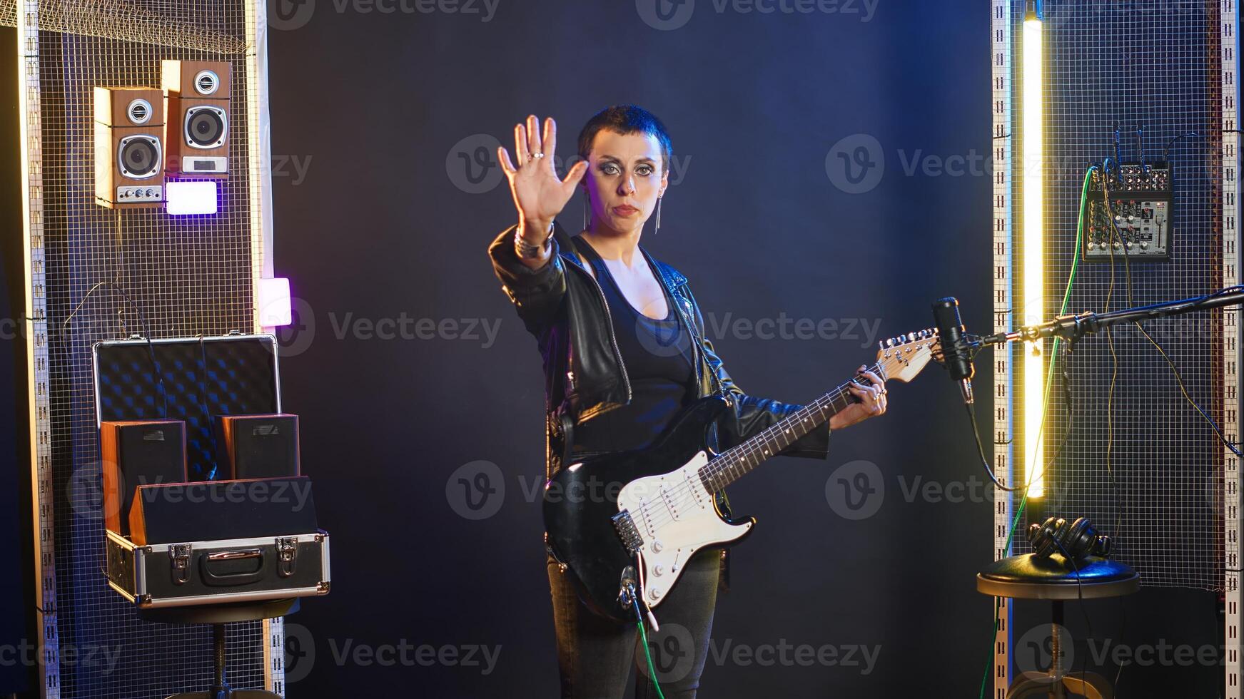 Superstar musician showing the stop sign with her palm to express rejection and restrictions, electric guitar and an edgy grunge style. Female artist singer showing refusal and no symbol. Camera B. photo