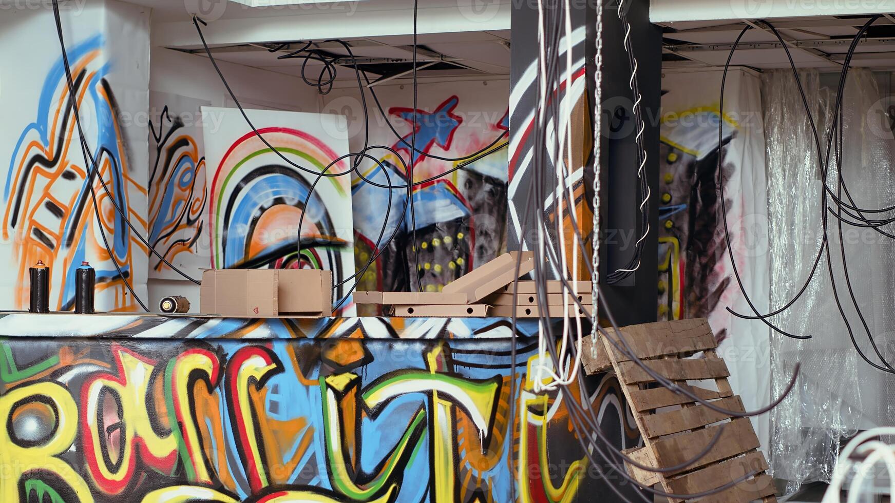Panning shot of spraying paint cans in defaced building with colorful graffiti art on walls. Pizza boxes left over in messy underground criminal den used as headquarters by teenagers photo