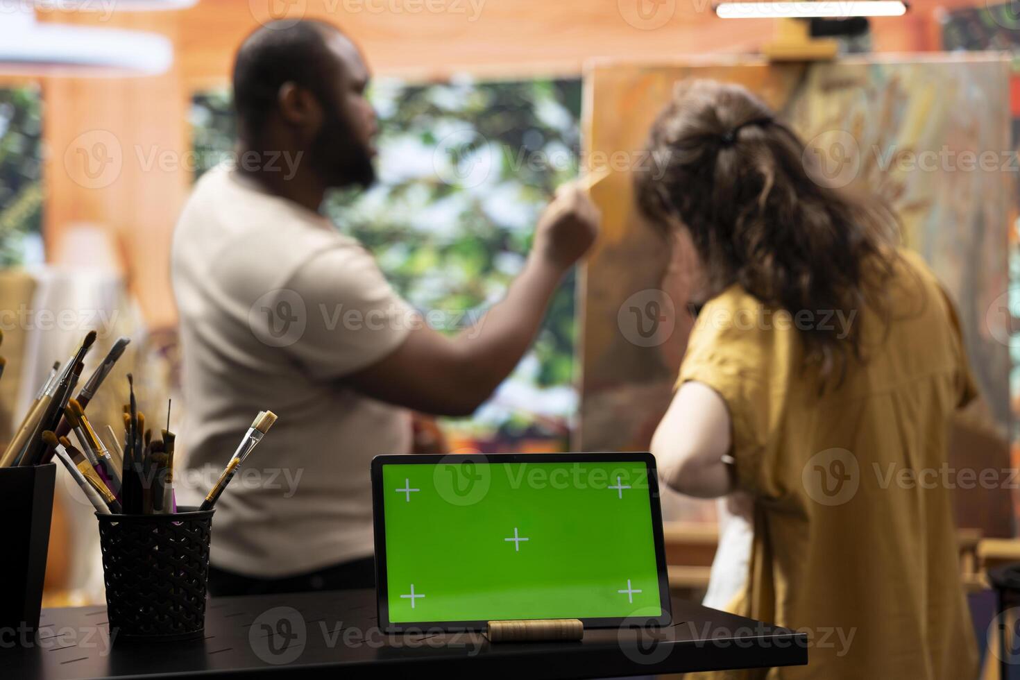 Skilled painters working on an artistic creation next to chroma key screen, using watercolor paint and brush kit to create a masterpiece. Two diverse artists enjoying their creative hobby. photo
