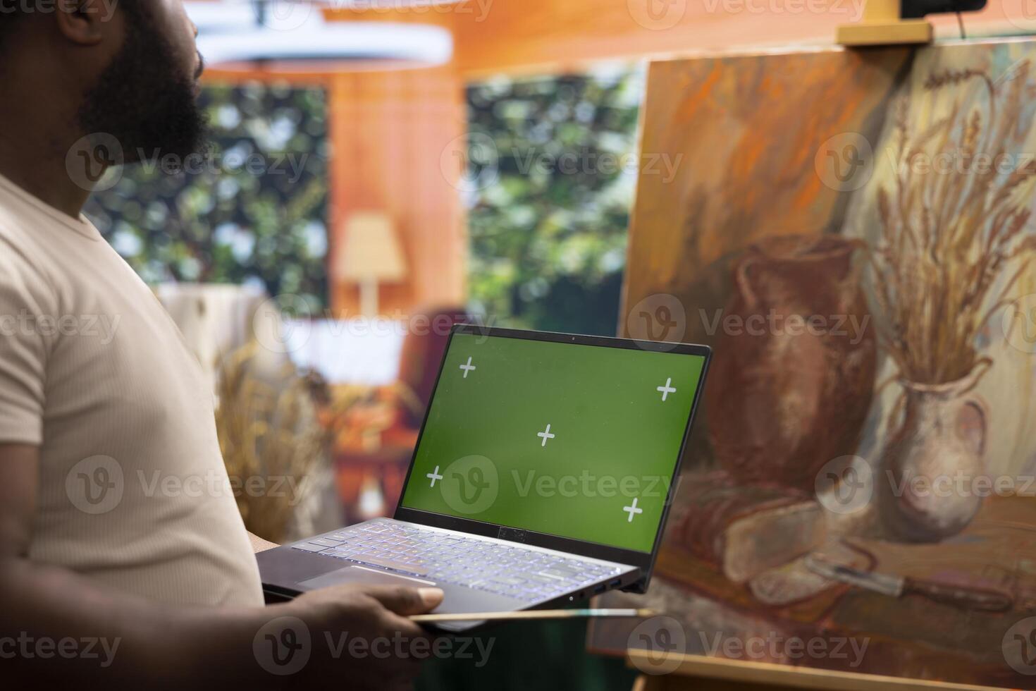 African american artist holding device with green screen mockup in art studio, working on a new painting with a certain technique. Painter using watercolor and acrylic dye for his creation. photo