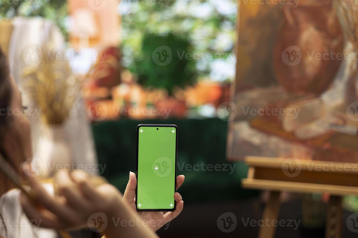 Young woman looking at chroma key display and at her rustic masterpiece, feeling proud and confident with her paintwork for the art gallery. Artist enjoying her hobby for leisure. photo