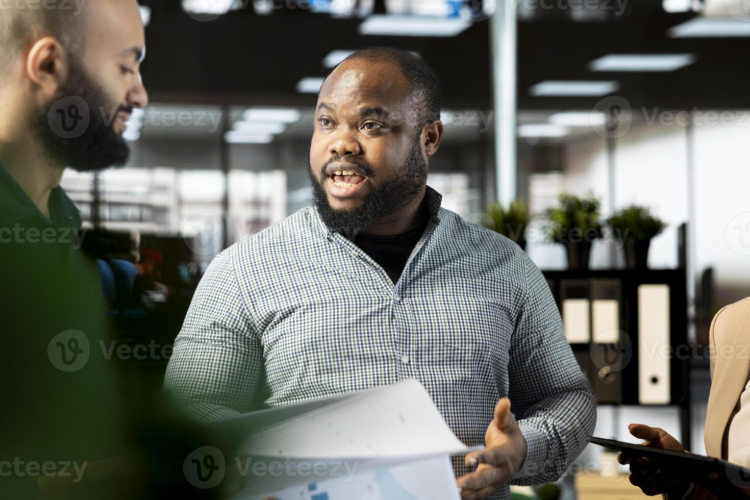 African american employee in company office checking progress on customer commissioned project. Man collaborating with colleague, comparing key data statistics after business audit photo
