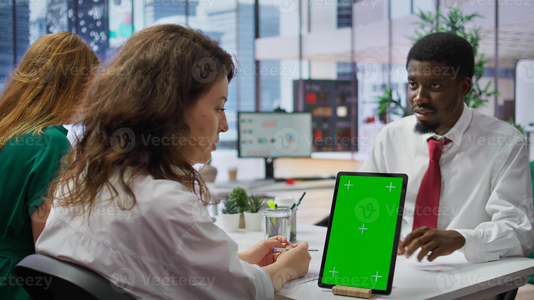 Job applicant and employer discussing in an interview with isolated mockup display on a device, high end corporate office. Businessman and HR recruiter share career development ideas. Camera B. photo