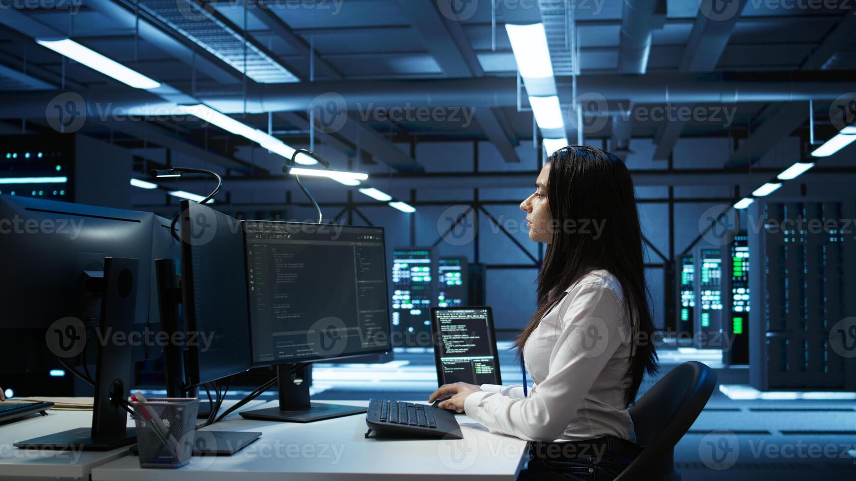 Engineer in data center sitting down at desk, installing software on computer, troubleshooting issues. Woman arriving at work in server hub, establishing performance benchmarks, camera B photo