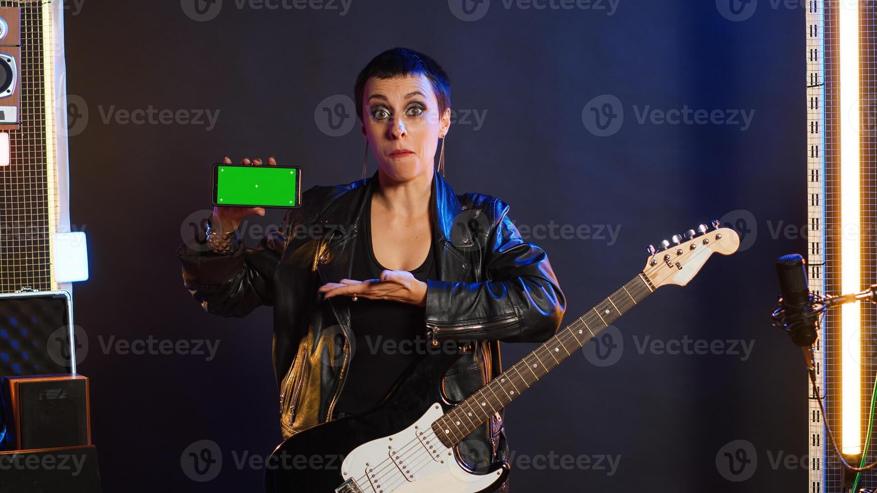 Cool rebellious rock star does a live performance pointing to copy space screen at nightclub, feeling powerful in her leather jacket and dark make up. Trendy powerful girl performing. Camera A. photo