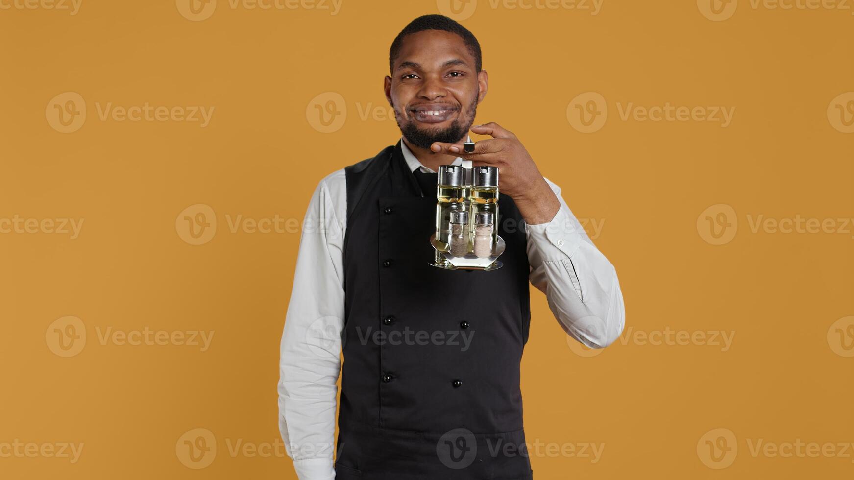 Skilled waiter showing a thumbs up symbol in front of the camera, presenting his approval and positive emotions in studio. Young restaurant staff gives a like or good sign. Camera B. photo
