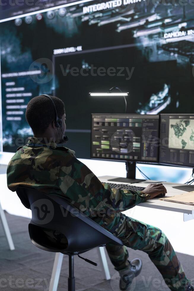 Army specialist working with advanced computer systems and cctv data for surveillance missions, gather intelligence to protect national interests. Strategic planning in a high tech control room. photo