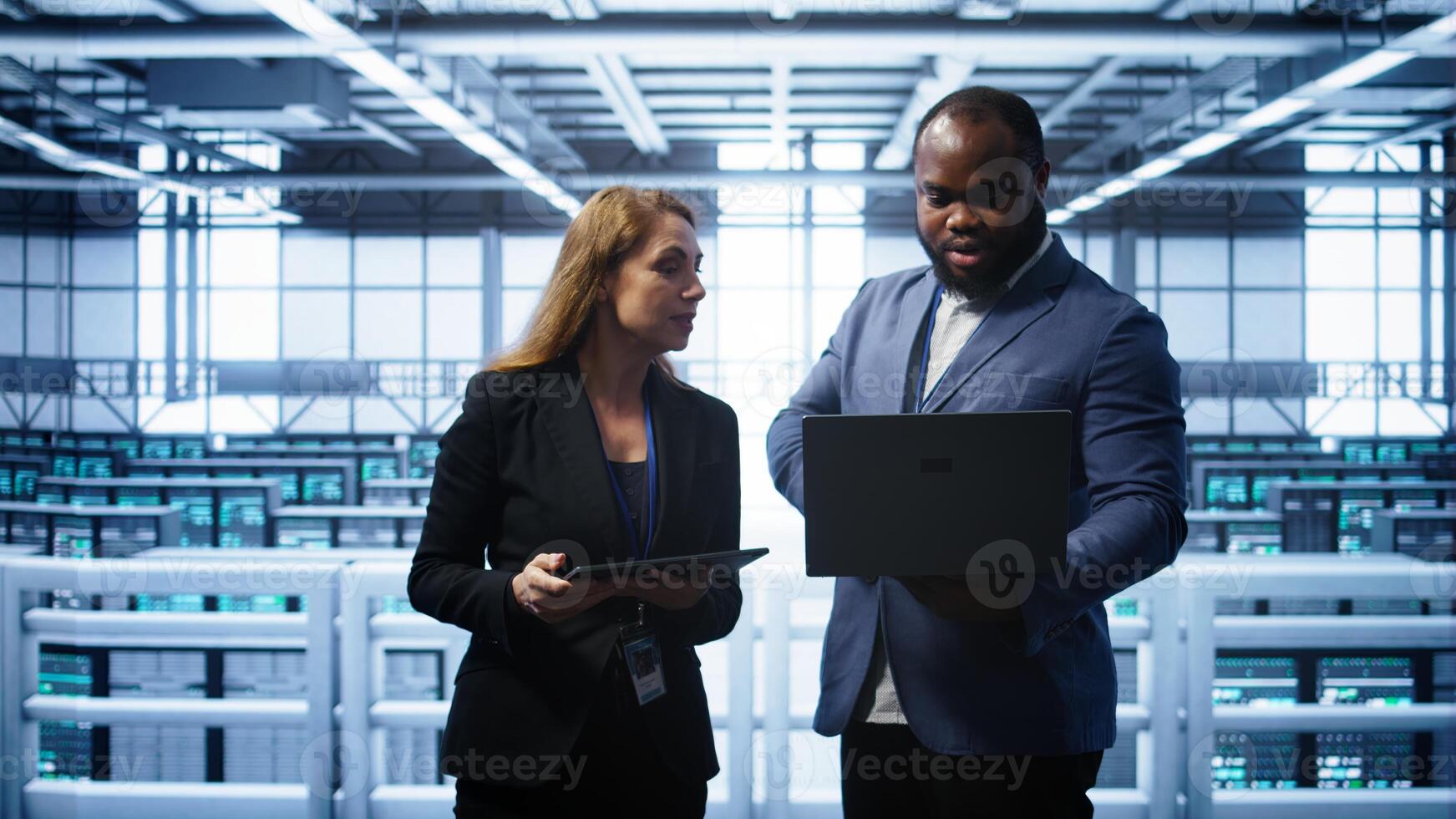 African american admin greeting inspector arriving in data center to supervise operations. IT expert in server hub workspace doing hand shake with supervisor monitoring performance, camera B photo