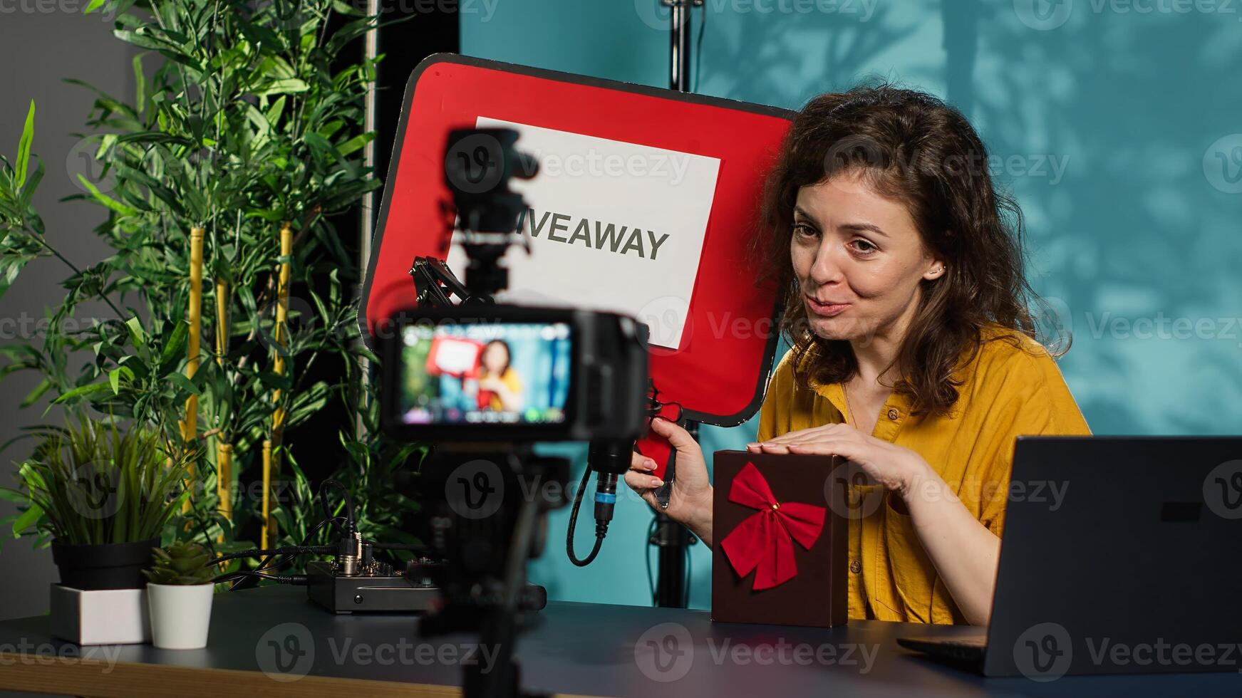 Media star holding empty copy space sign doing giveaway, offering packaged present. Woman does influencer marketing by offering prizes during internet contest, filming with professional gear, camera A photo