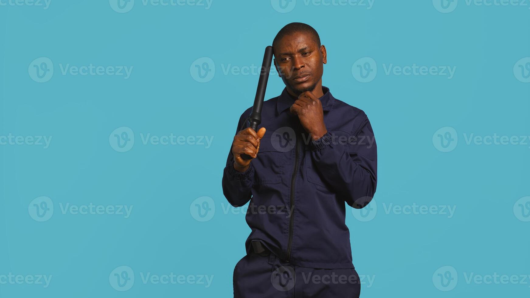 Portrait of security guard scratching head with baton while overseeing premises, thinking. Pensive private law enforcement worker daydreaming, rubbing chin, studio backdrop, camera B photo
