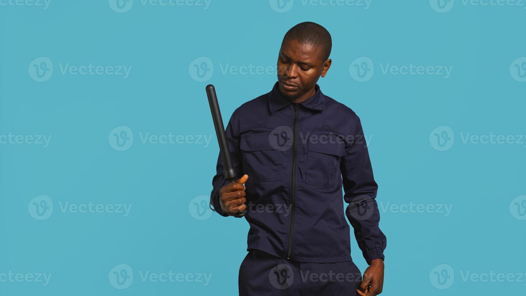 Security guard removing baton from belt, preparing to attack suspects. Portrait of bodyguard pointing finger towards truncheon, threatening to subdue criminals, studio background, camera B photo