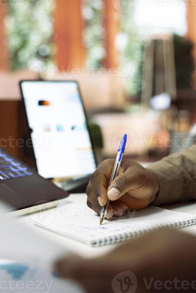Business owner writes monthly accounting balance numbers on a notebook, examining financial reports and statistics at home office. Entrepreneur calculates finance and economy data. Close up. photo