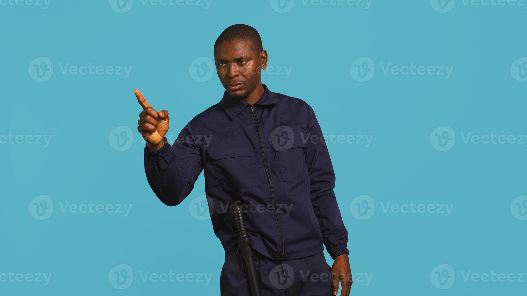 Portrait of security agent pointing finger at people, warning them while securing assigned post, studio background. African american guardian scolding trespassers, handling security breaches, camera B photo