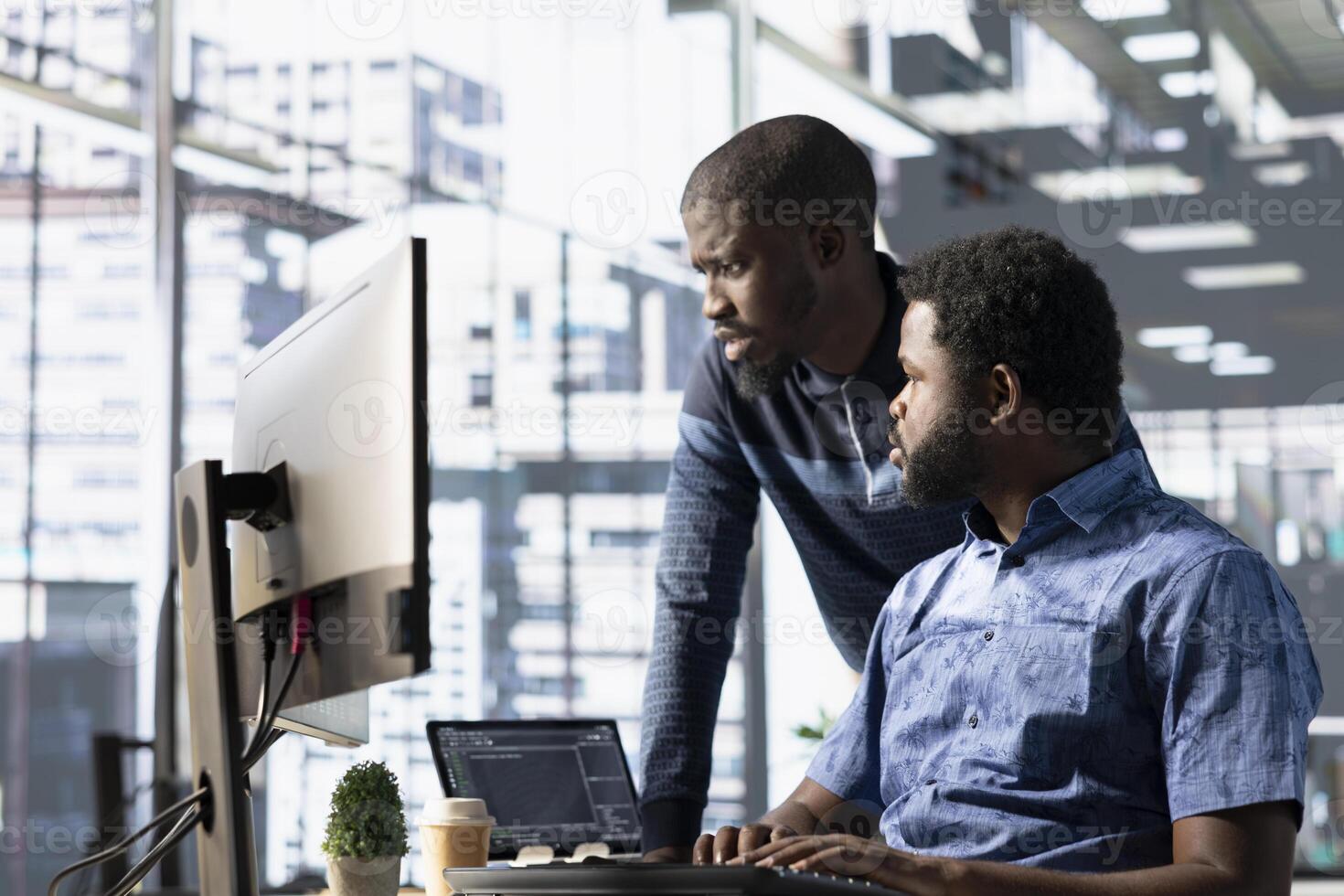 Data engineering IT staff members at PC desk developing machine learning algorithms. African american team in office solving tasks, training large scale deep learning models using computer photo