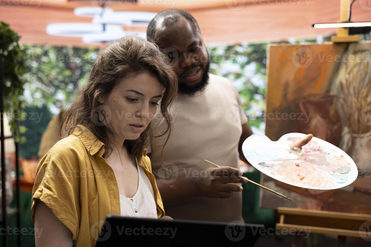 Team of painters searching inspiration for a rustic painting online using laptop in art studio, doing research and finding creativity to finish their masterpiece. Diverse artists in atelier. photo