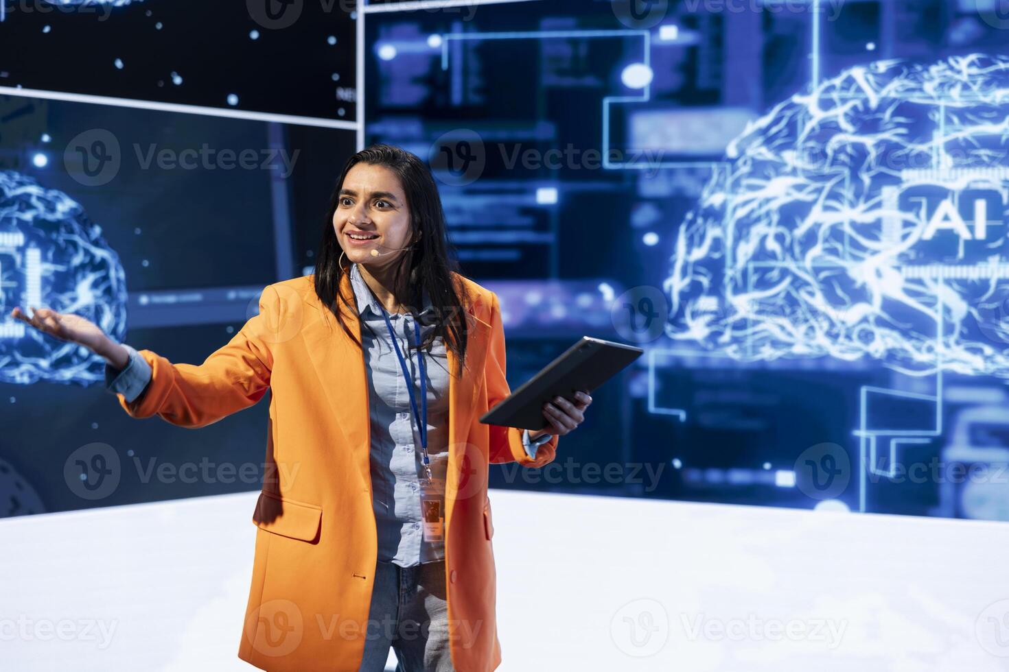 Woman using microphone and tablet to do presentation at workshop exploring developments in AI and machine learning. Technician on stage at artificial intelligence expo, holding speech photo