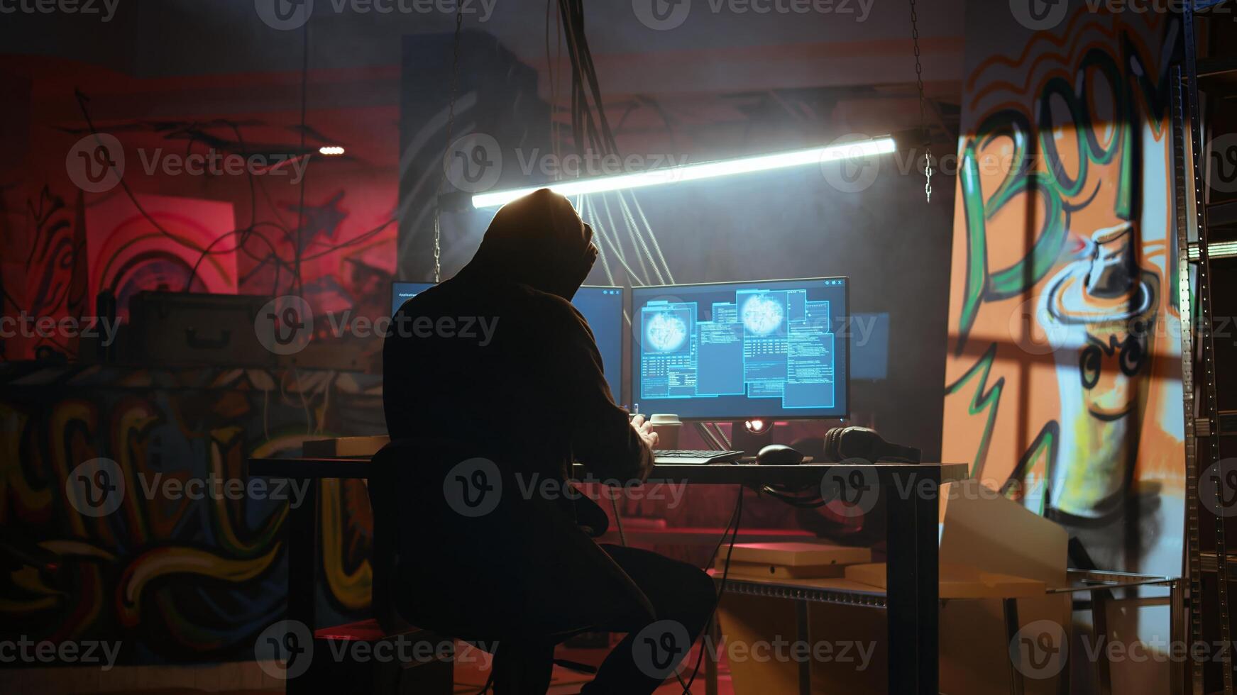 Hacker in hidden location with graffiti walls using PC to deploy malware on unsecured devices, stealing sensitive data from unaware users online and selling it on black market, jib down shot photo
