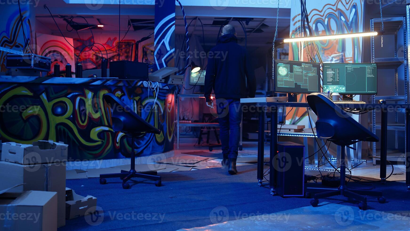 Hooded hacker arrives in neon lit underground shelter filled with graffiti artwork. Cybercriminal enters colorful painted basement, starting work on script that can crash businesses servers, camera A photo