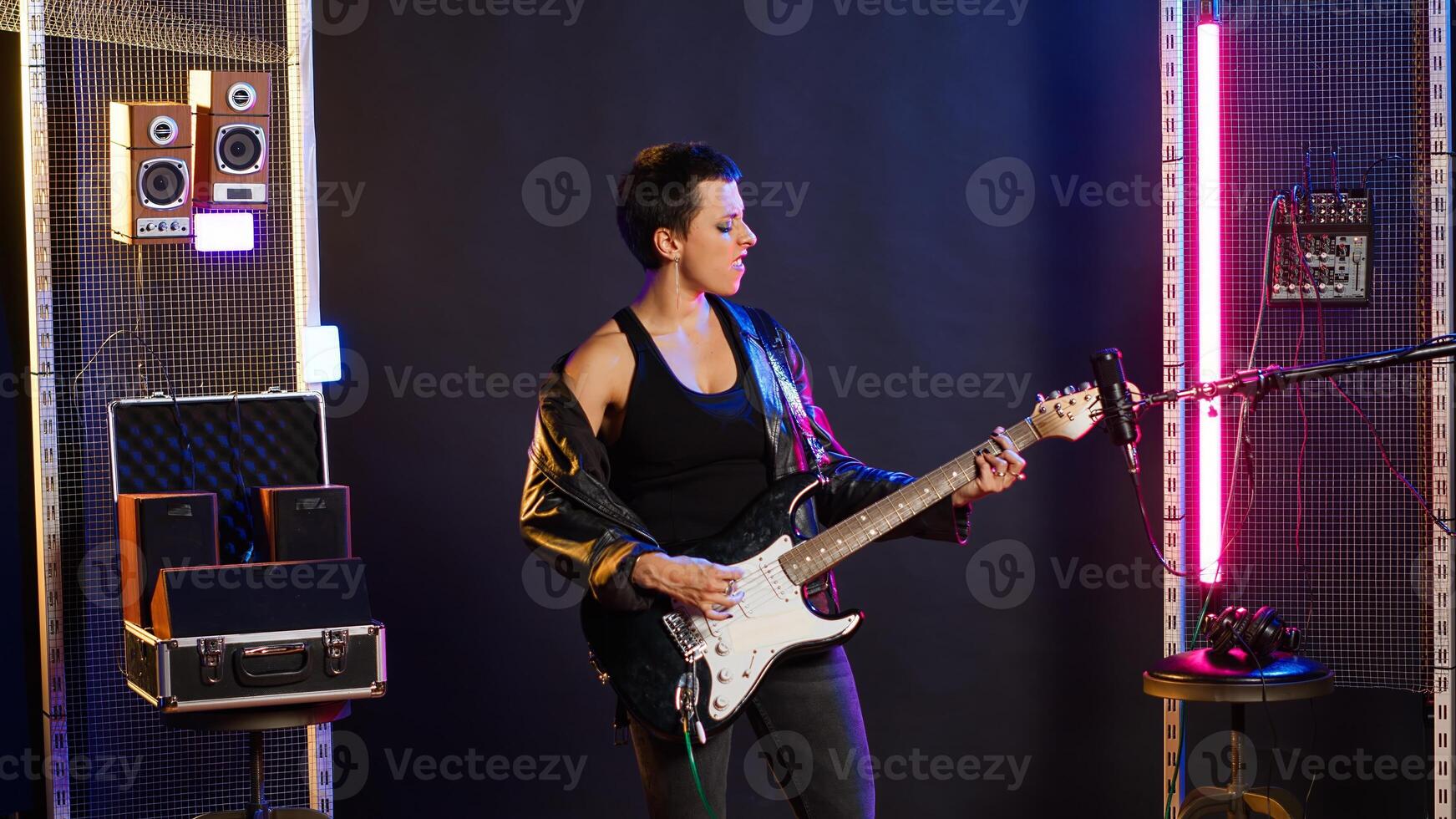 Woman performer showing thumbs up symbol and playing guitar, edgy grunge music performance in studio. Female rocker artist giving her approval with a positive like sign. Camera B. photo