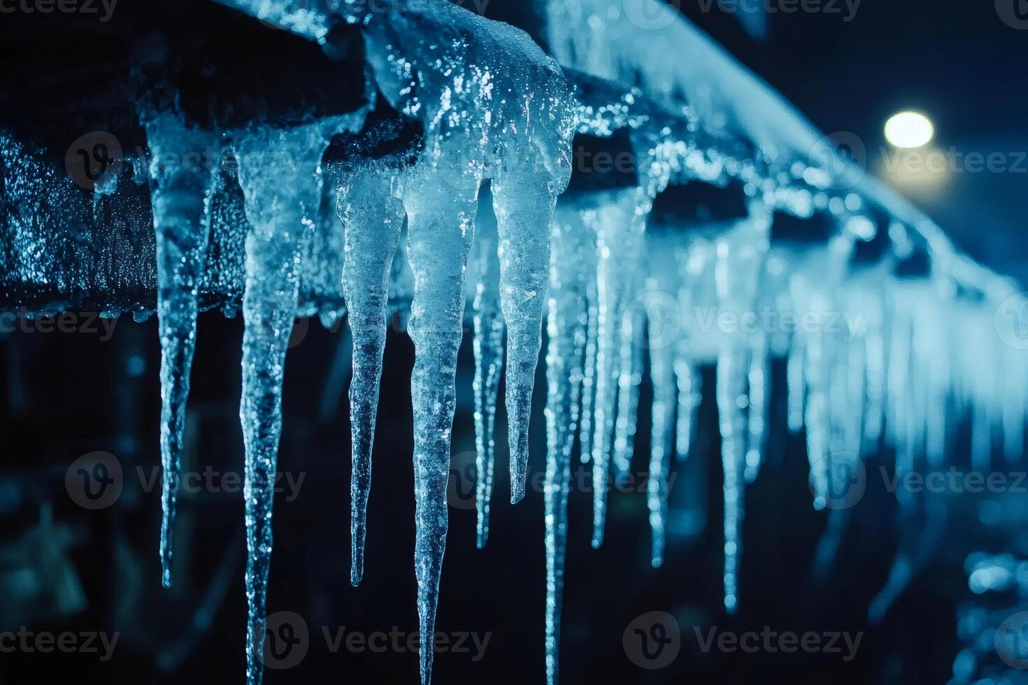 Sharp icicles hanging from roof at night during winter season photo