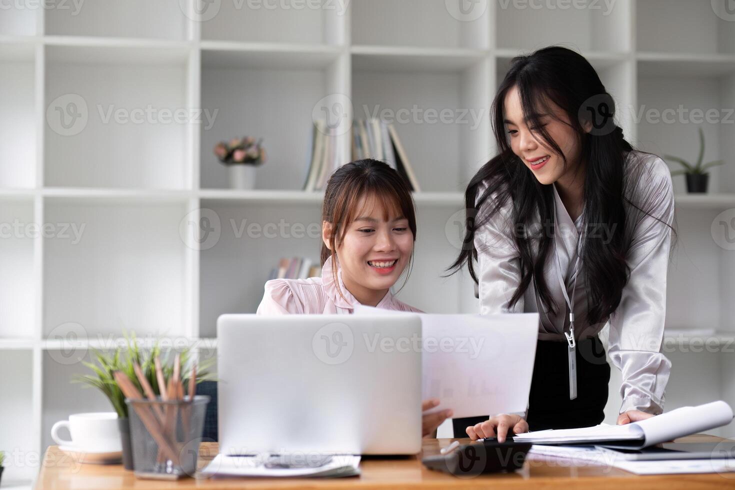 Two Asian businesswomen discuss business planning ideas on work desks in the office. photo