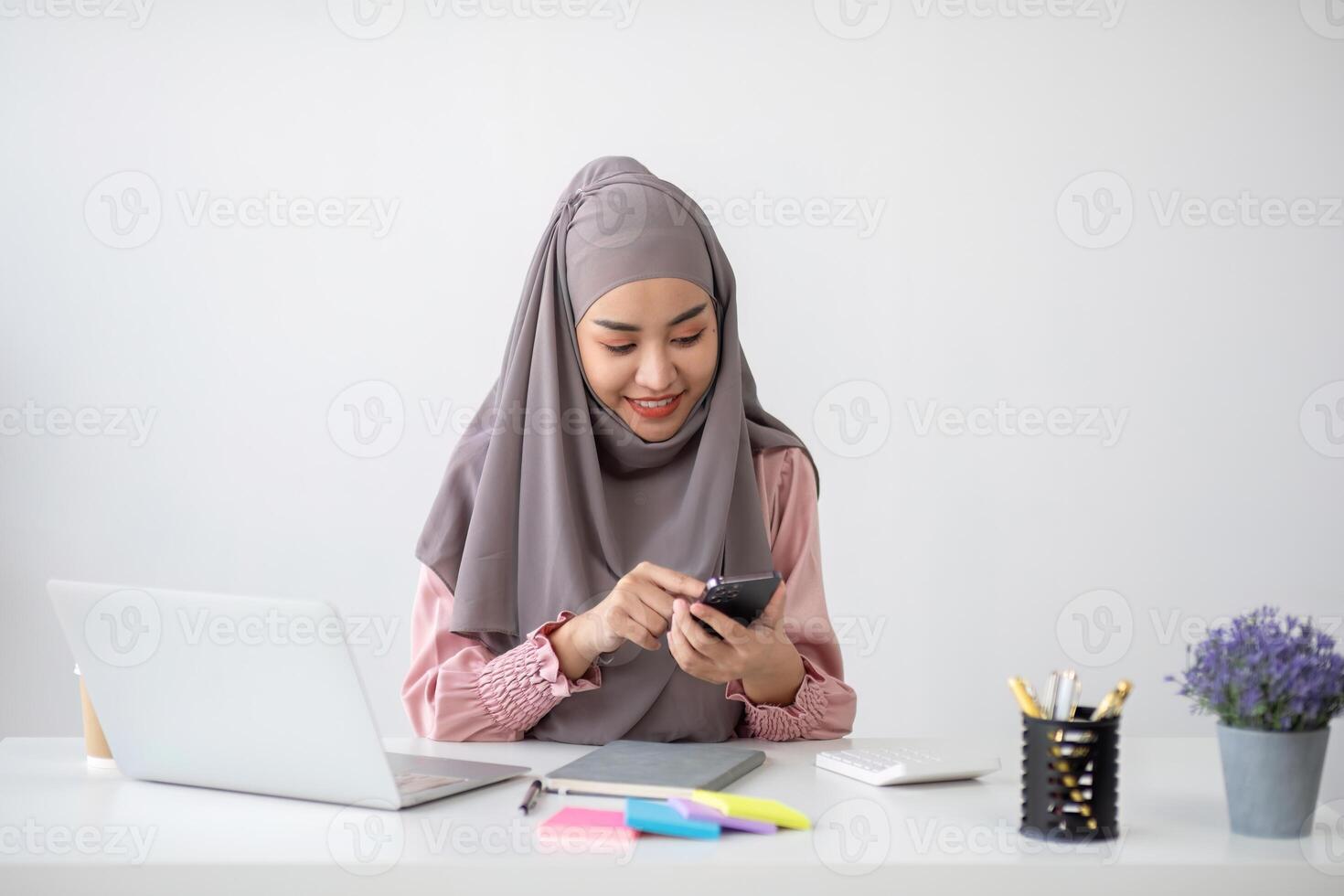 Smiling Muslim business woman Wearing a hijab while chatting online on a work desk in the office. photo