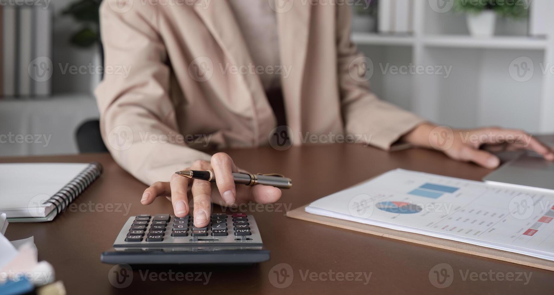 Young female accountant is calculating business and financial figures using a calculator. On the wooden table in the office photo