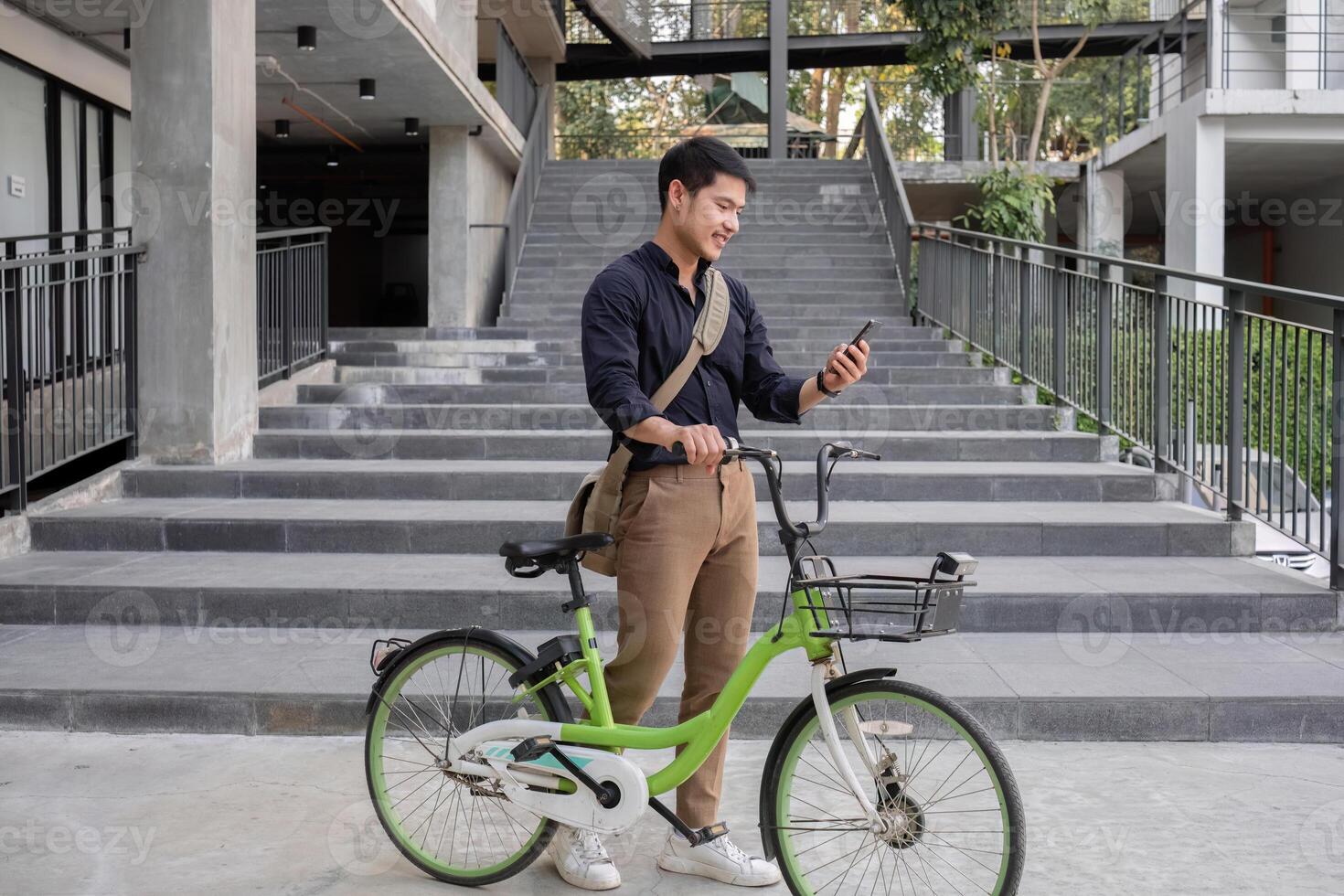 A young Asian businessman rides a bicycle to work. Standing outside the office talking on the phone and talking about business. Concept of reducing energy and reducing air pollution. photo