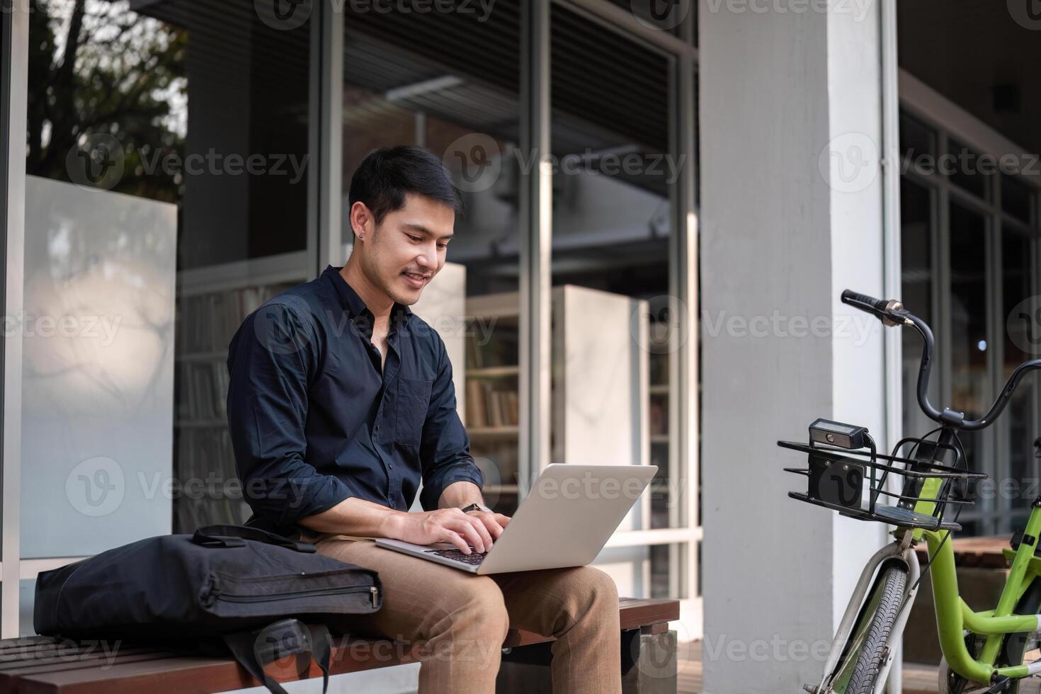 A young Asian businessman rides a bicycle to work. Use a reusable water bottle. Working outside of the office using a laptop The concept of saving energy and reducing pollution to the environment. photo